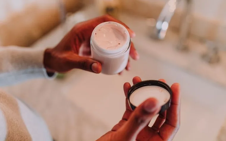A tube of moisturizer and a jar of body cream on a bathroom shelf