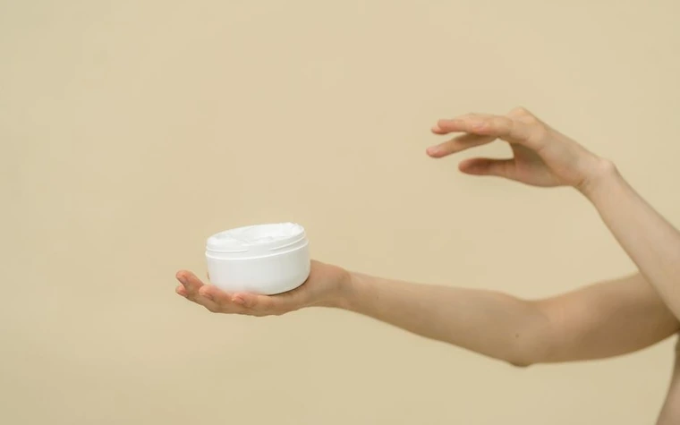 A hand holding a small cream jar next to bare skin
