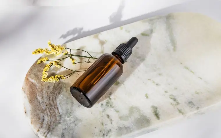 Dropper bottle of facial serum on a marble surface with dried flowers
