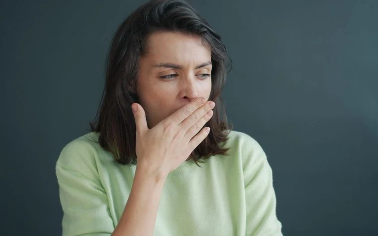 A young woman yawning and covering her mouth, looking tired