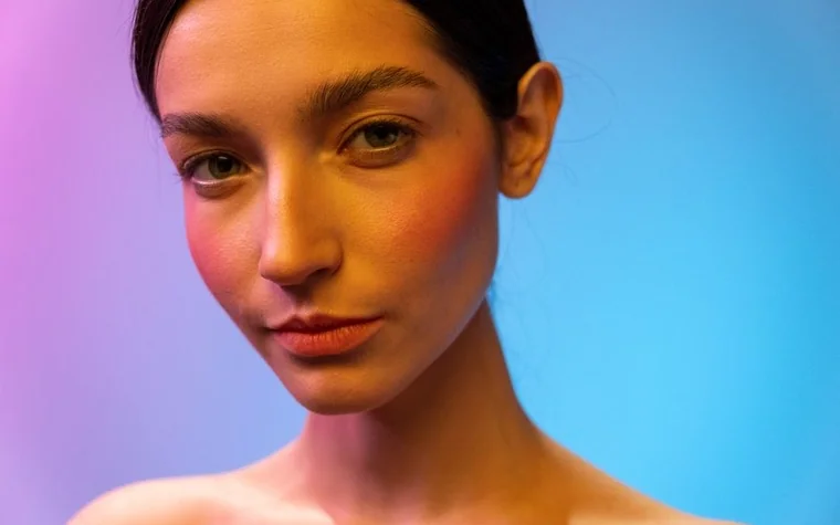 Close-up portrait of a woman's face under colorful pink and blue studio lighting