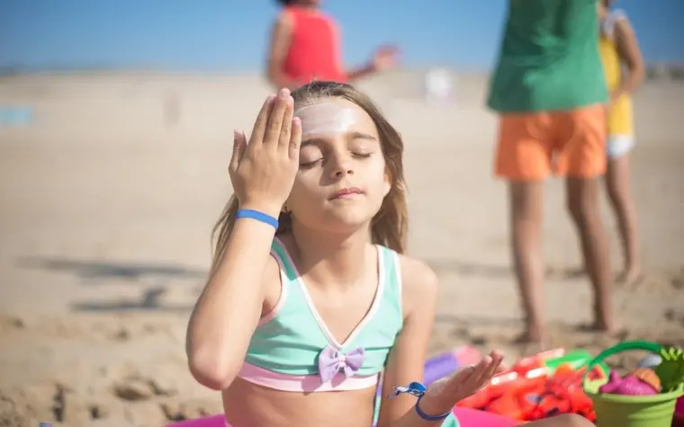 Young girl at the beach applying sunscreen to her forehead with eyes closed