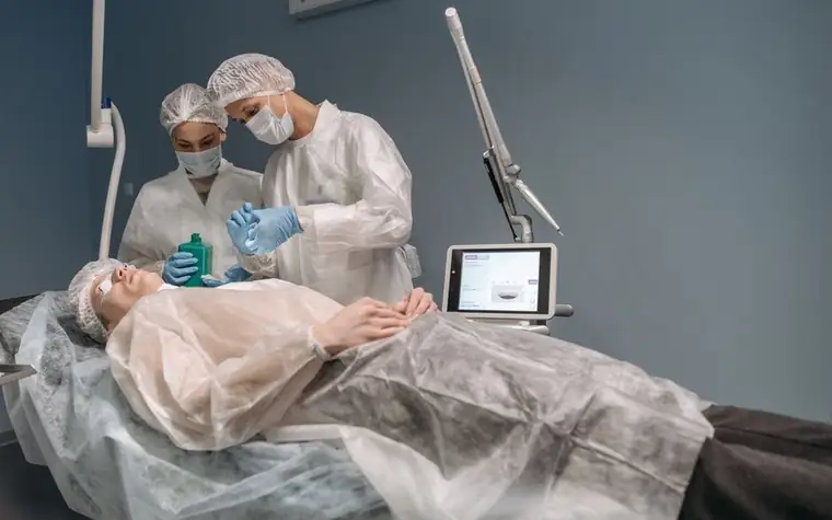 Two dermatology staff in protective gowns performing a skin treatment on a patient