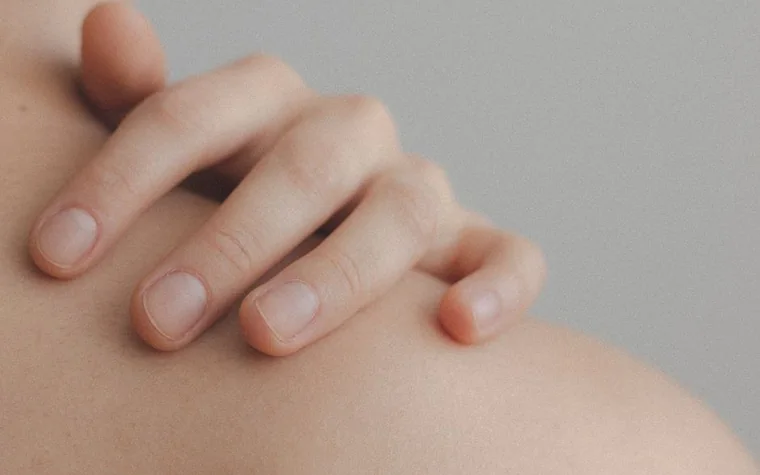 Close-up of a hand resting gently on a bare shoulder, showing natural skin texture
