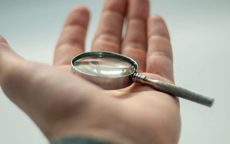 Hand holding a magnifying glass against a pale blue background