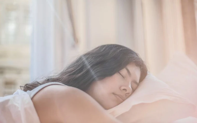 A young woman with curly hair sleeping peacefully in a bed with a knit blanket