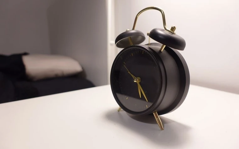 A black vintage alarm clock on a white bedside table
