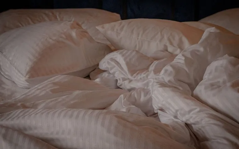 Rumpled white sheets and pillows on an unmade bed