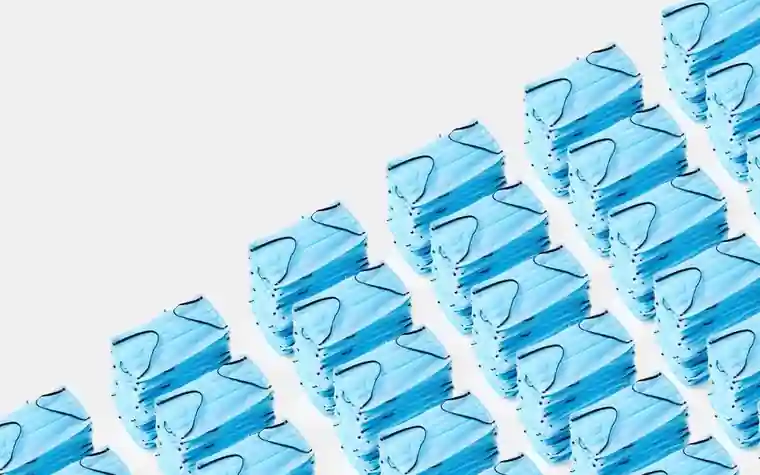 Rows of blue disposable surgical face masks stacked in a diagonal pattern on a white background