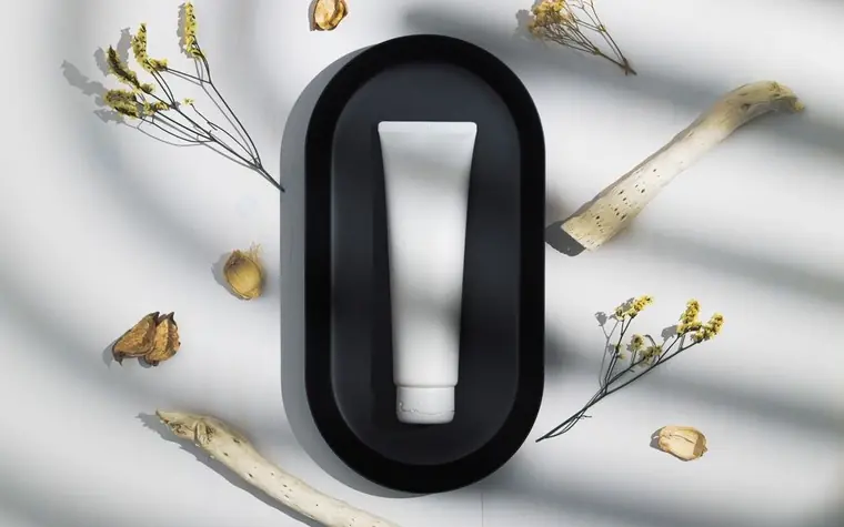 White skincare tube standing in a black oval holder among dried flowers and plant stems
