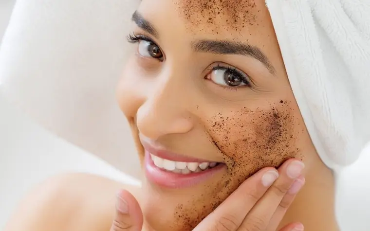 Smiling woman with a towel on her head and exfoliating scrub particles on her cheek