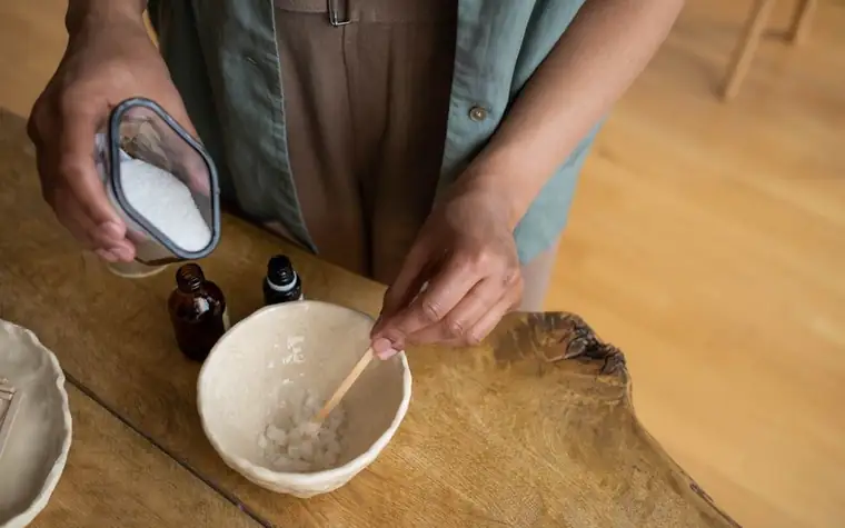 Hands pouring white granules into a bowl to mix a homemade scrub