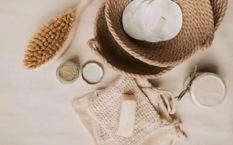 Flat lay of a bristle body brush, mesh bag and small jars on a beige surface