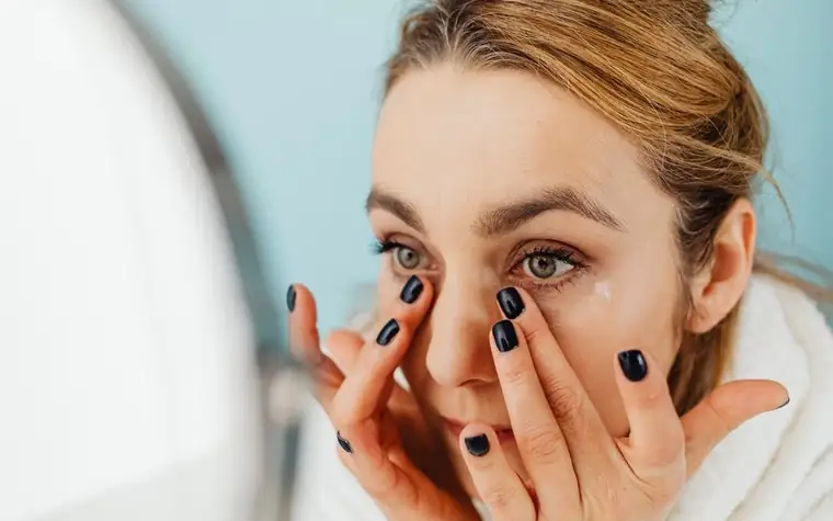 A woman examining her under-eye area in a mirror
