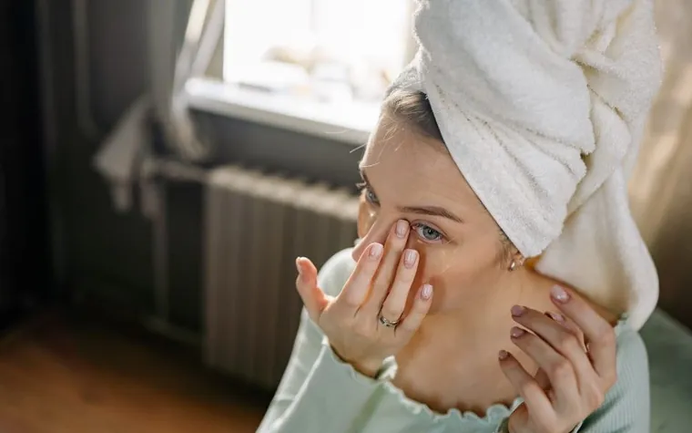 A woman applying skincare to her face by a window