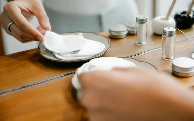 A cotton pad and small skincare bottles on a wooden vanity