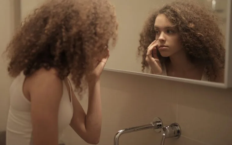 A woman examining her face in a bathroom mirror