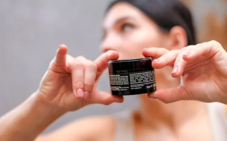 A woman holding a cosmetic cream jar and reading its label