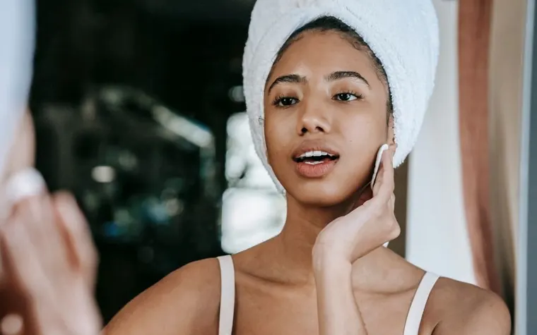 A woman applying a cotton pad to her cheek during a skincare routine