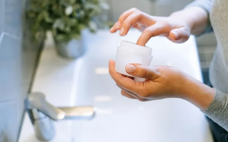 Close-up of hands applying face cream from a jar