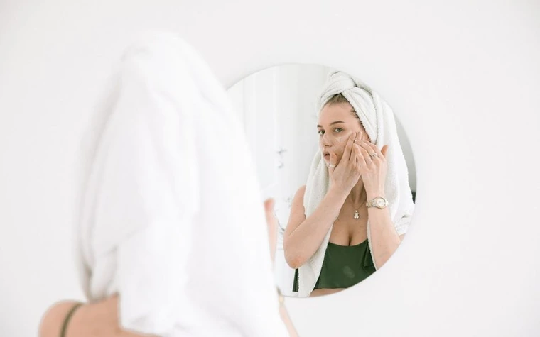 A woman applying face cream while looking in a mirror