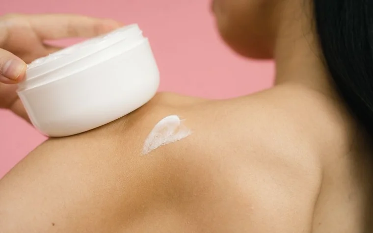 A woman applying moisturizing cream to her shoulder