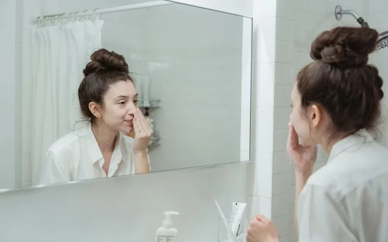 A woman in a bathroom applying a skincare product to her face