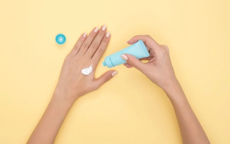 Cream being squeezed from a tube onto a hand against a yellow background