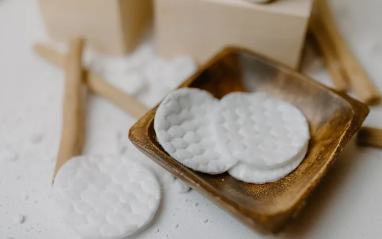 A wooden dish holding round cotton exfoliating pads for skincare