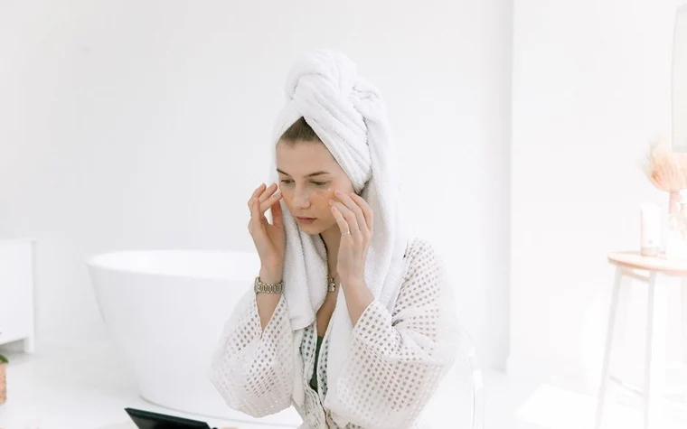 A woman in a robe applying an exfoliating treatment to her face