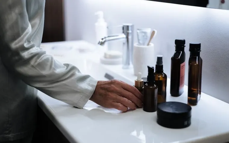 A hand reaching for skincare products on a bathroom shelf