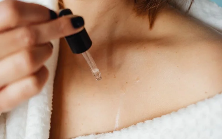 A woman applying a few drops of serum to her collarbone area