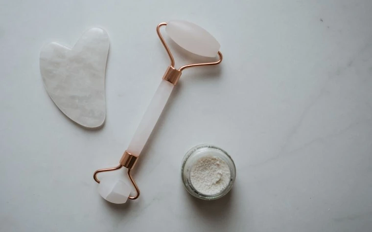 A flat lay of a gua sha tool, facial roller, and skincare jar