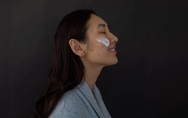 A woman with her eyes closed and moisturizer applied to her cheek