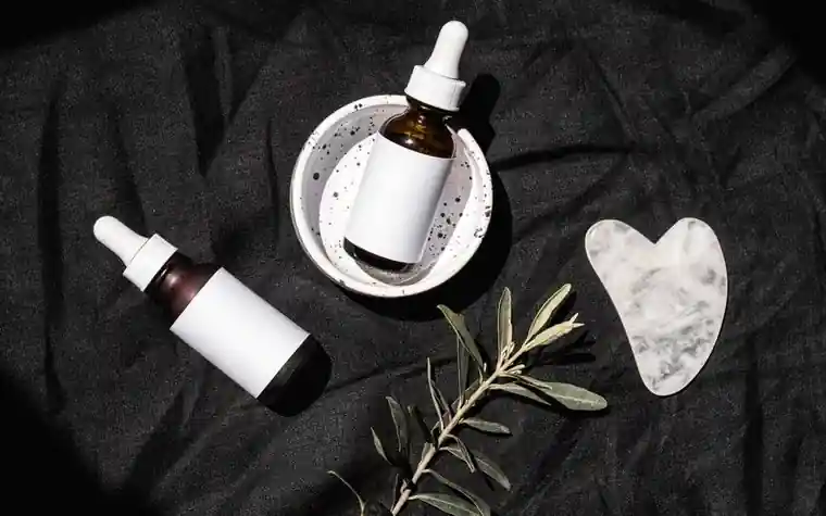An elegant flat lay of amber skincare bottles and a gua sha stone on a marble surface