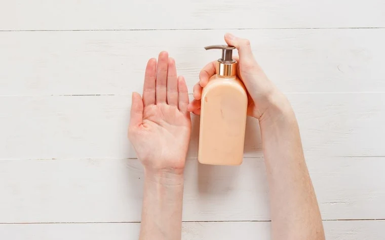 A top-down view of hands applying lotion from a pump bottle