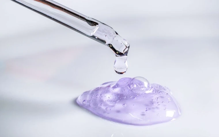 A pipette releasing a drop of gel against a light background
