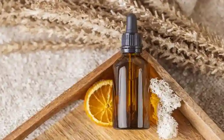 A dropper bottle of serum resting beside a sliced orange on a wooden surface