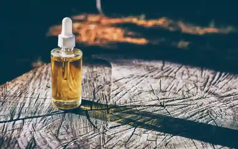 A dropper bottle of golden serum resting on a tree stump in sunlight
