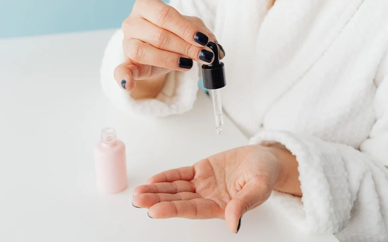 A woman applying serum from a dropper to her cheek