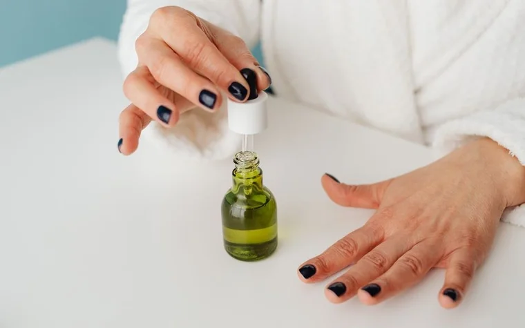 A hand using a dropper to apply a green serum
