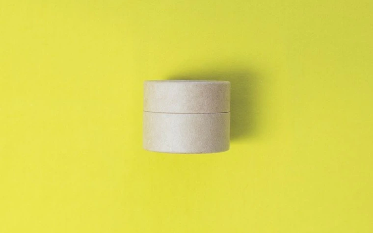 A brown cosmetic jar with lid open against a yellow background