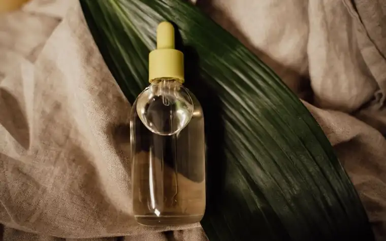 Manicured hands using a dropper to dispense a green liquid serum