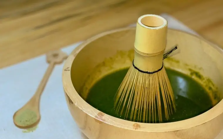 Bamboo whisk in a wooden bowl preparing matcha tea