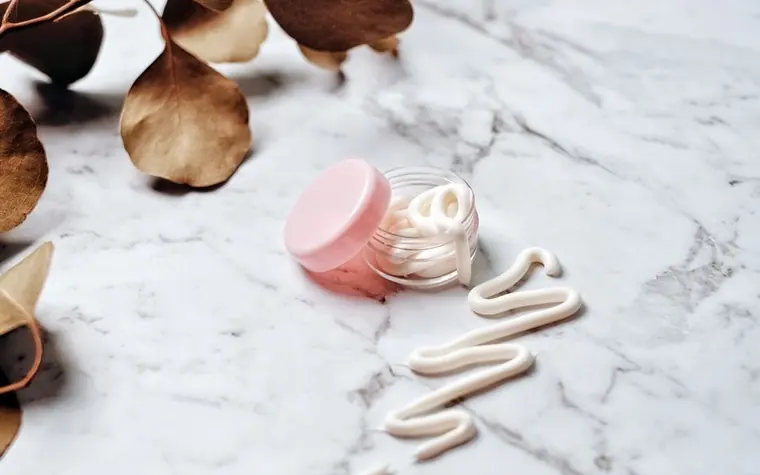 A small pink cosmetic jar on a marble surface with dried leaves