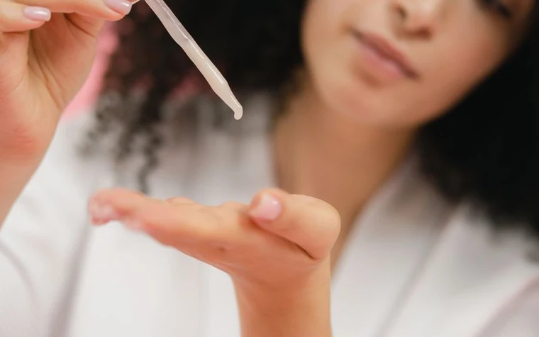 A woman applying serum to her face with a glass pipette