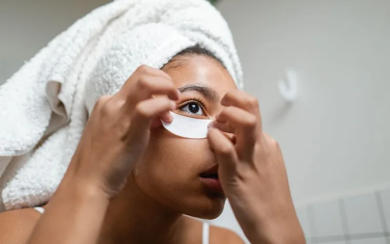 A woman applying under-eye patches during a skincare routine