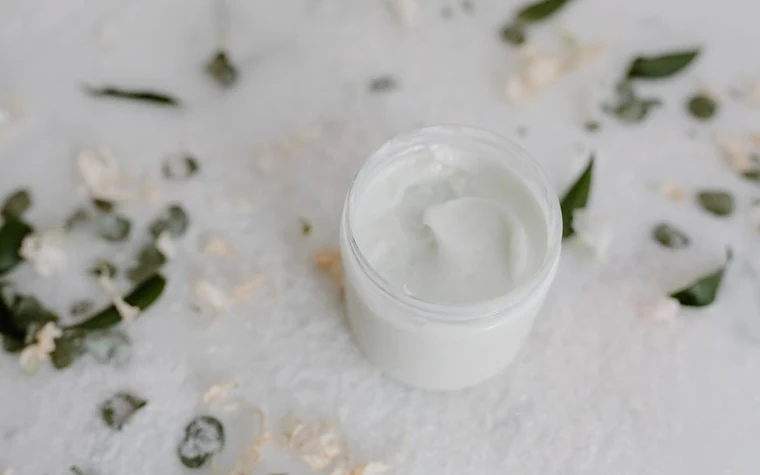 An open jar of white cream surrounded by white flowers