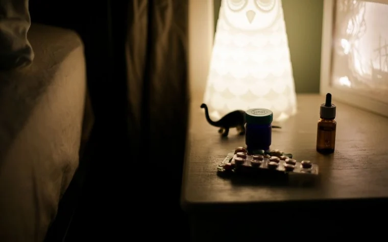 A dimly lit bedside table at night with a small amber bottle and a warm lamp, evoking a nighttime skincare routine