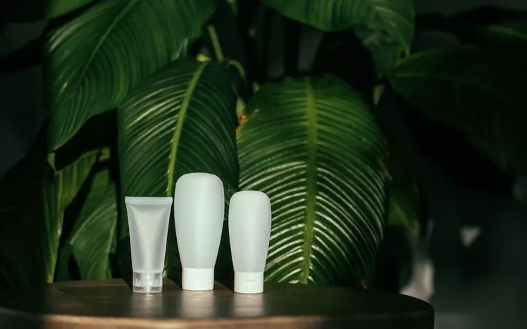 White cosmetic tube containers against a green leaf backdrop